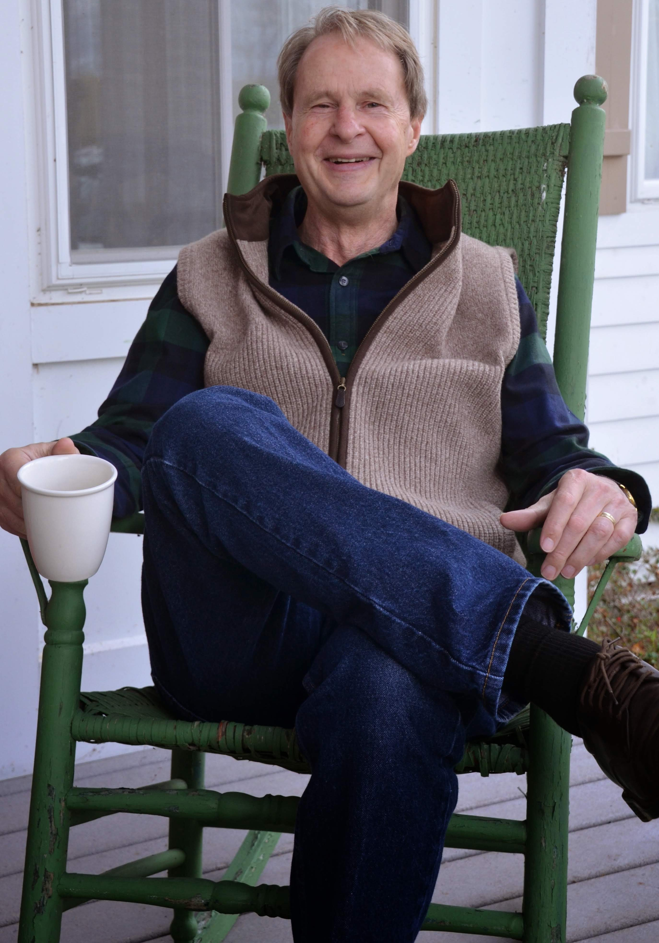 Joseph Goering, smiling with a mug outside on a green rocking chair