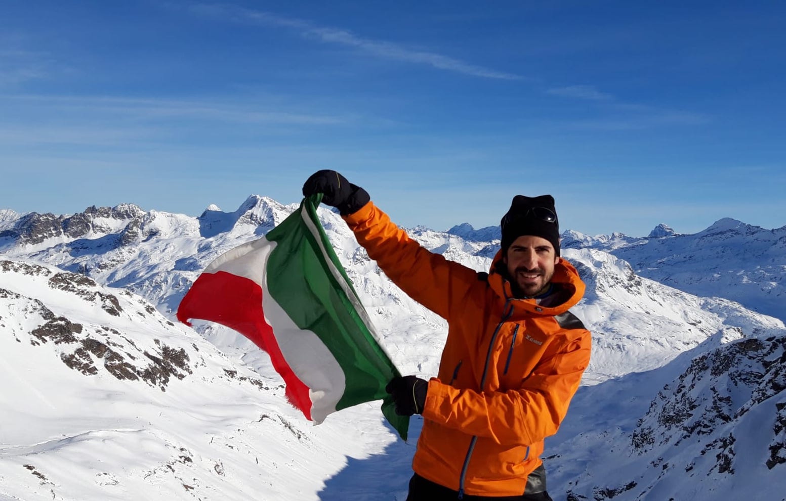 Riccardo Macchioro waving an Italian flag atop a snowy mountain